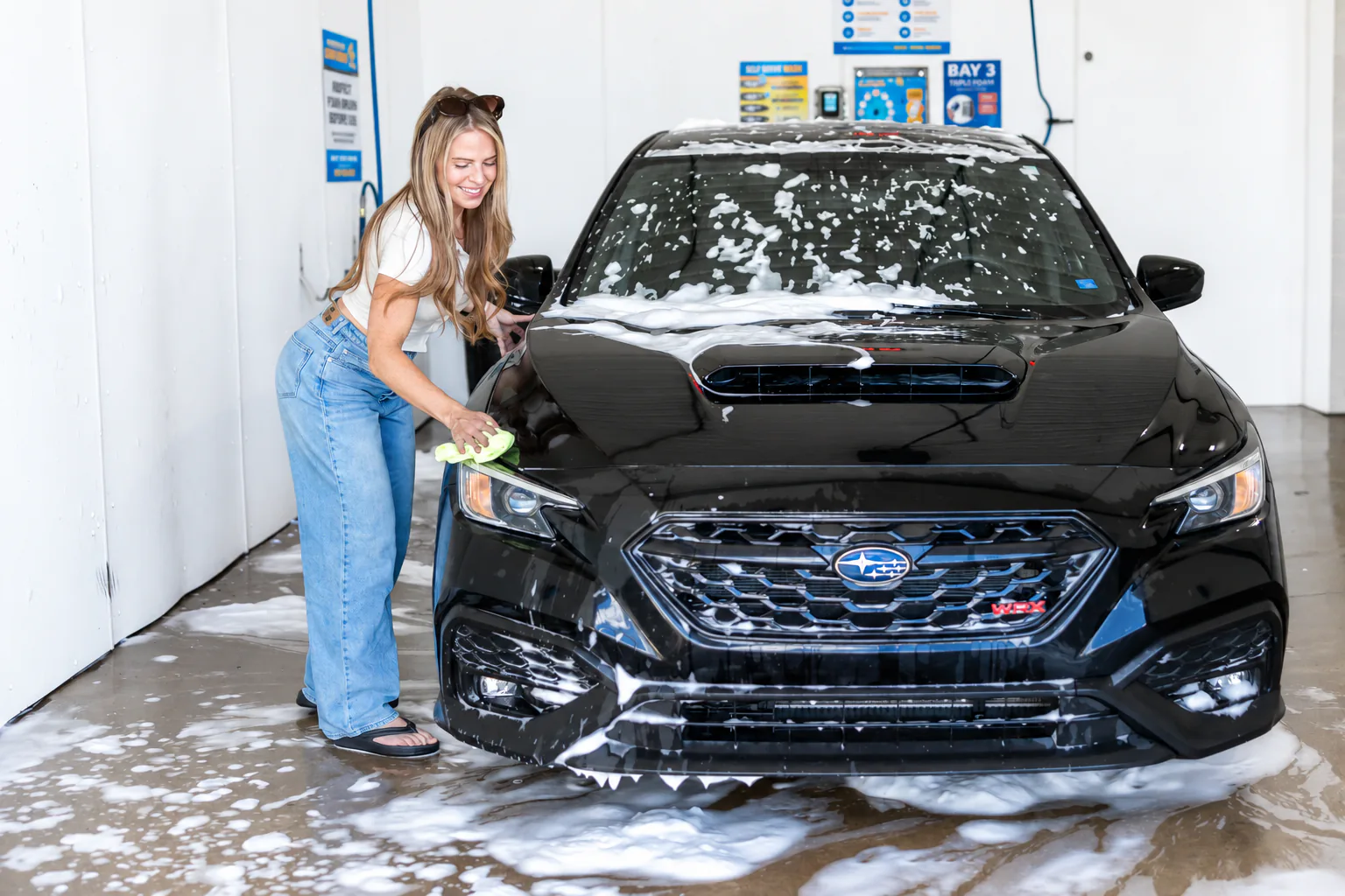 A customer wiping down her foam-covered car in a Rubber Duck self-serve bay